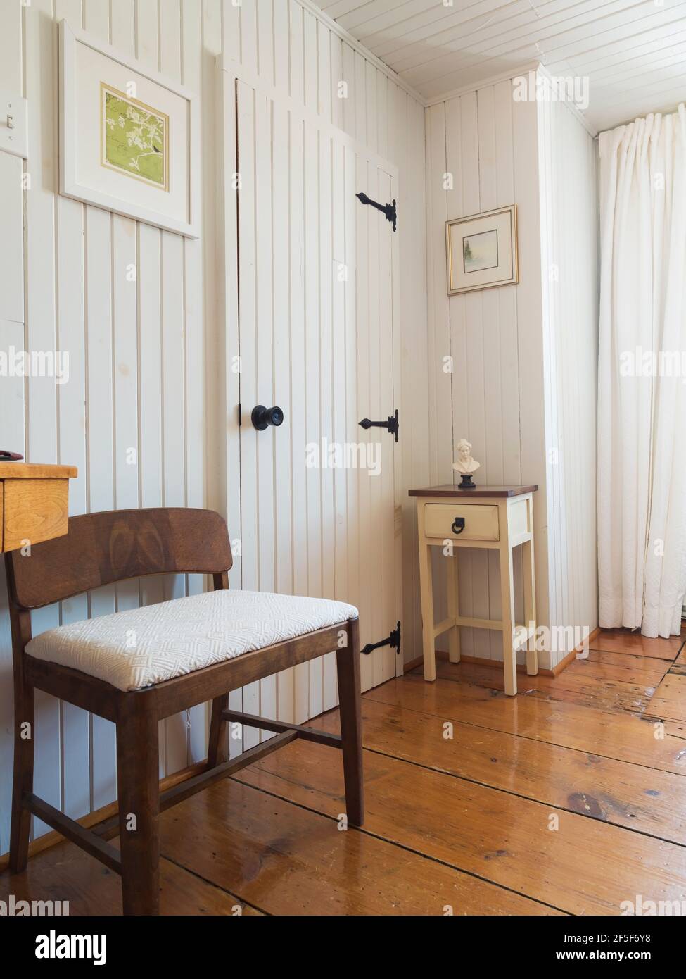 Stuhl mit niedriger Rückenlehne mit gepolstertem Sitz aus weißem Stoff,  kleiner Nachttisch aus Holz neben der Schranktür im Hauptschlafzimmer mit  breitem Pinien-Holzboden Stockfotografie - Alamy