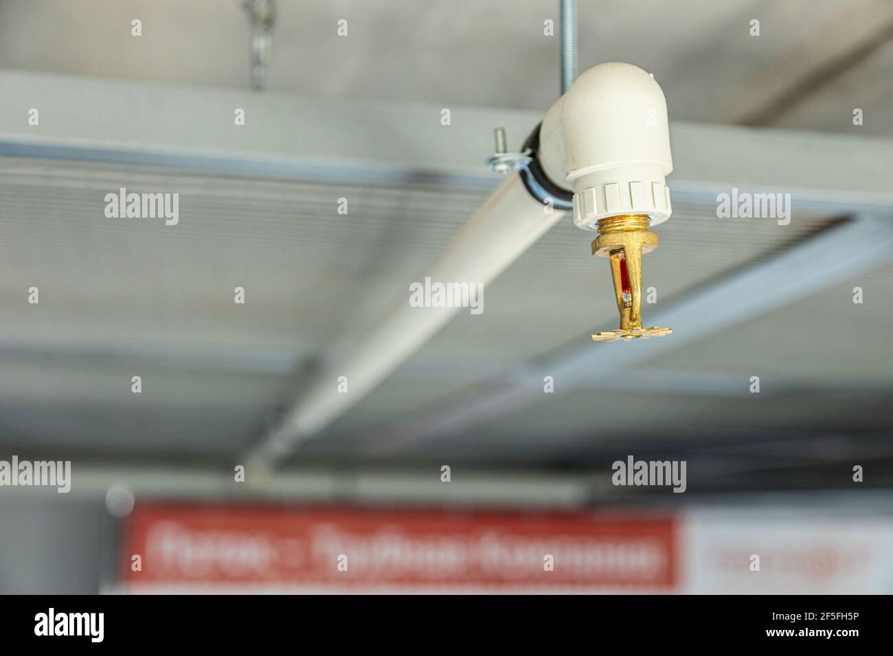 Nahaufnahme des Sprinklerschutzes mit Feuer im Hintergrund. Die Sprinkler sind Teil einer integrierten Wasserleitung, die für Leben und Feuer ausgelegt ist Stockfoto