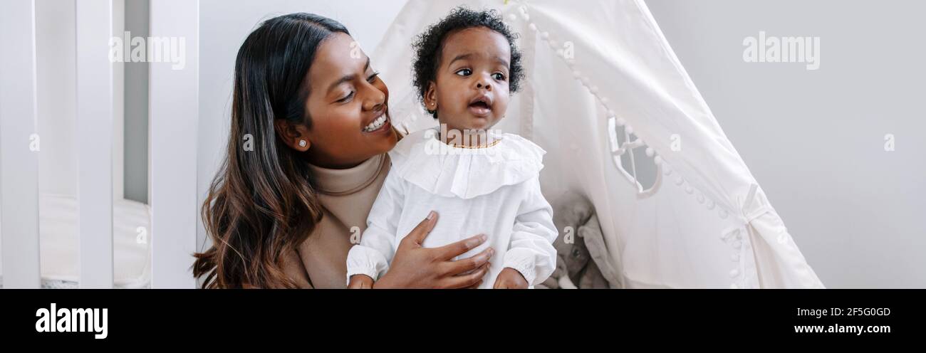 Glücklich lächelnd junge indische Mutter spielt mit einem schwarzen Baby Mädchen Tochter. Authentische glückliche Familie gemischt Rennen Menschen Mutter und Kind zusammen umarmt Stockfoto