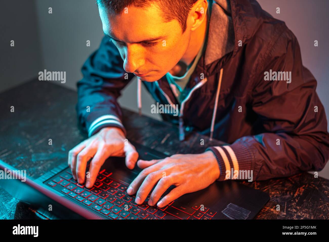 Ein männlicher Hacker tippt auf einer Laptop-Tastatur in einem dunklen Raum unter einem Neonlicht. Das Konzept von Cyberkriminalität Betrug und Identitätsdiebstahl Stockfoto