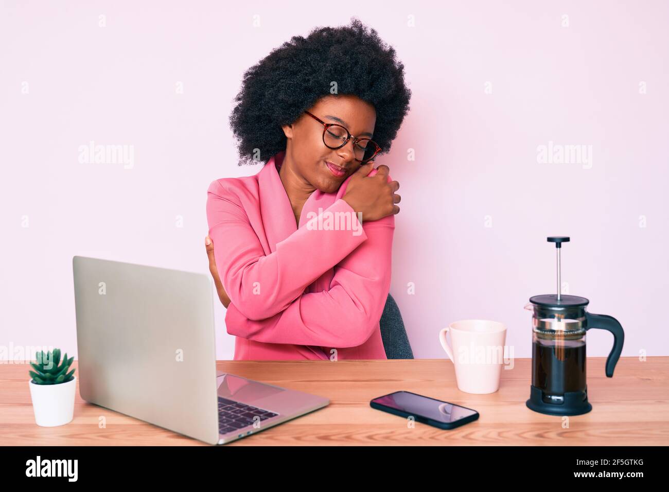 Junge afroamerikanische Frau arbeitet am Schreibtisch mit Computer-Laptop umarmt sich glücklich und positiv, lächelnd zuversichtlich. Selbstliebe und Selbstversorgung Stockfoto