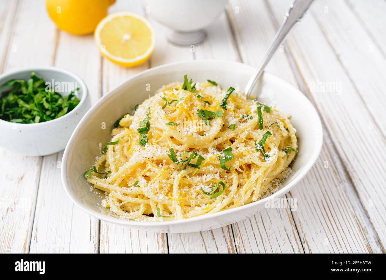 Pasta al Limone, köstliche italienische Mahlzeit, Spaghetti mit Parmesan, Butter und Zitronensauce, gekrönt mit frisch geriebener Schale und Käse auf rustikalem Holz BA Stockfoto