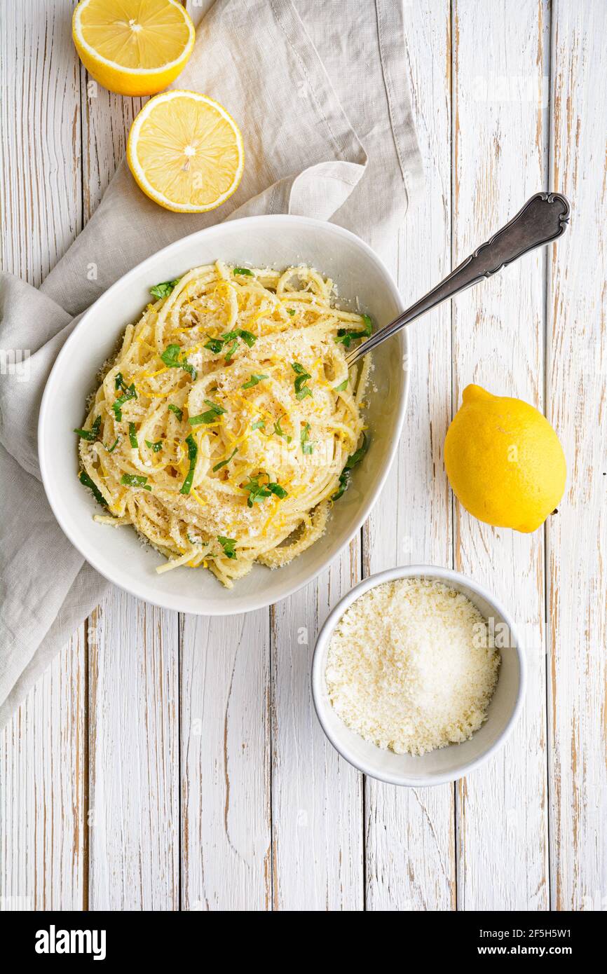 Pasta al Limone, köstliche italienische Mahlzeit, Spaghetti mit Parmesan, Butter und Zitronensauce, gekrönt mit frisch geriebener Schale und Käse auf rustikalem Holz BA Stockfoto