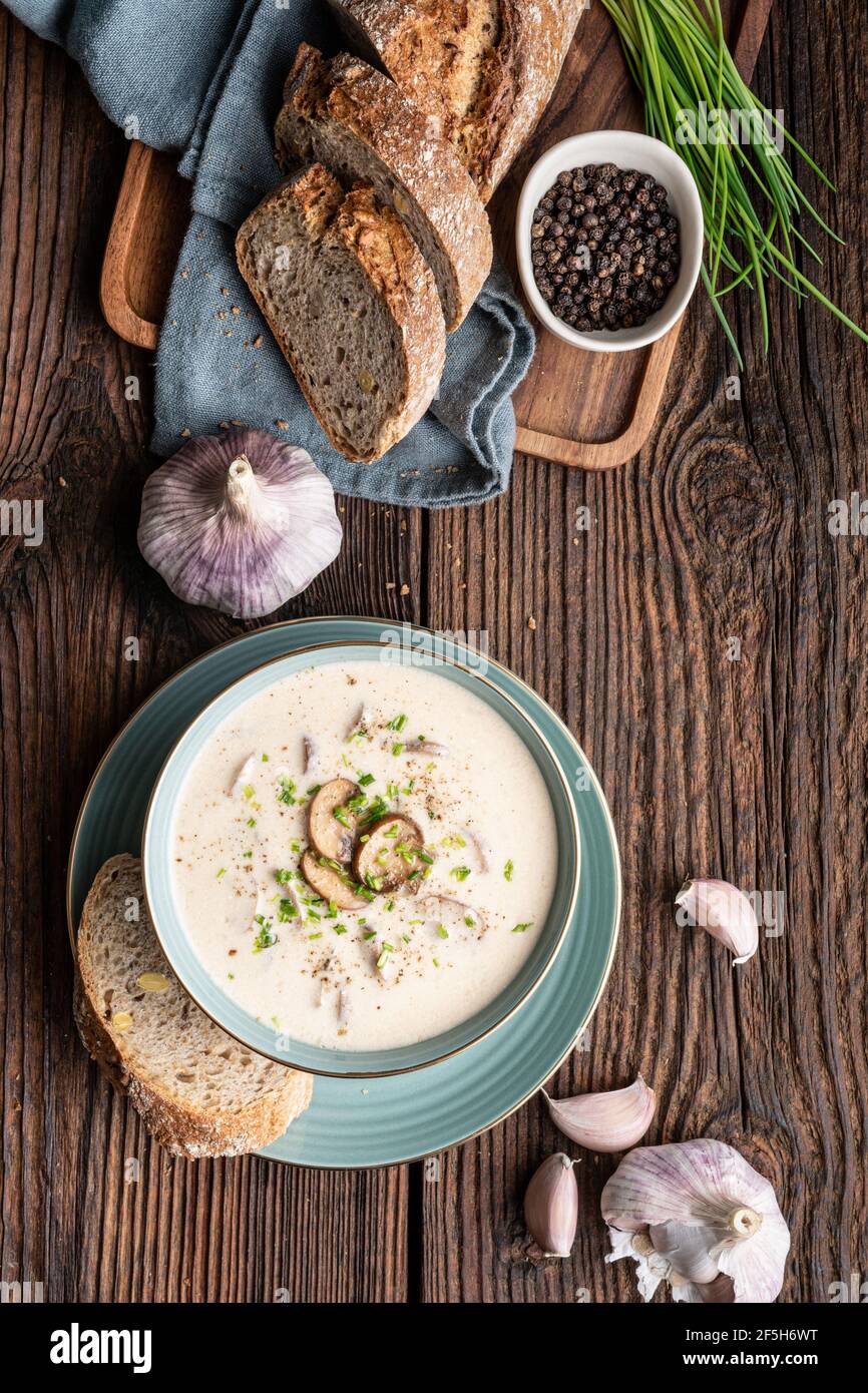 Köstliches Mittagessen, beruhigende Pilzsuppe mit frisch gehacktem Schnittlauch, serviert mit knusprigem Brot auf rustikalem Holzhintergrund Stockfoto