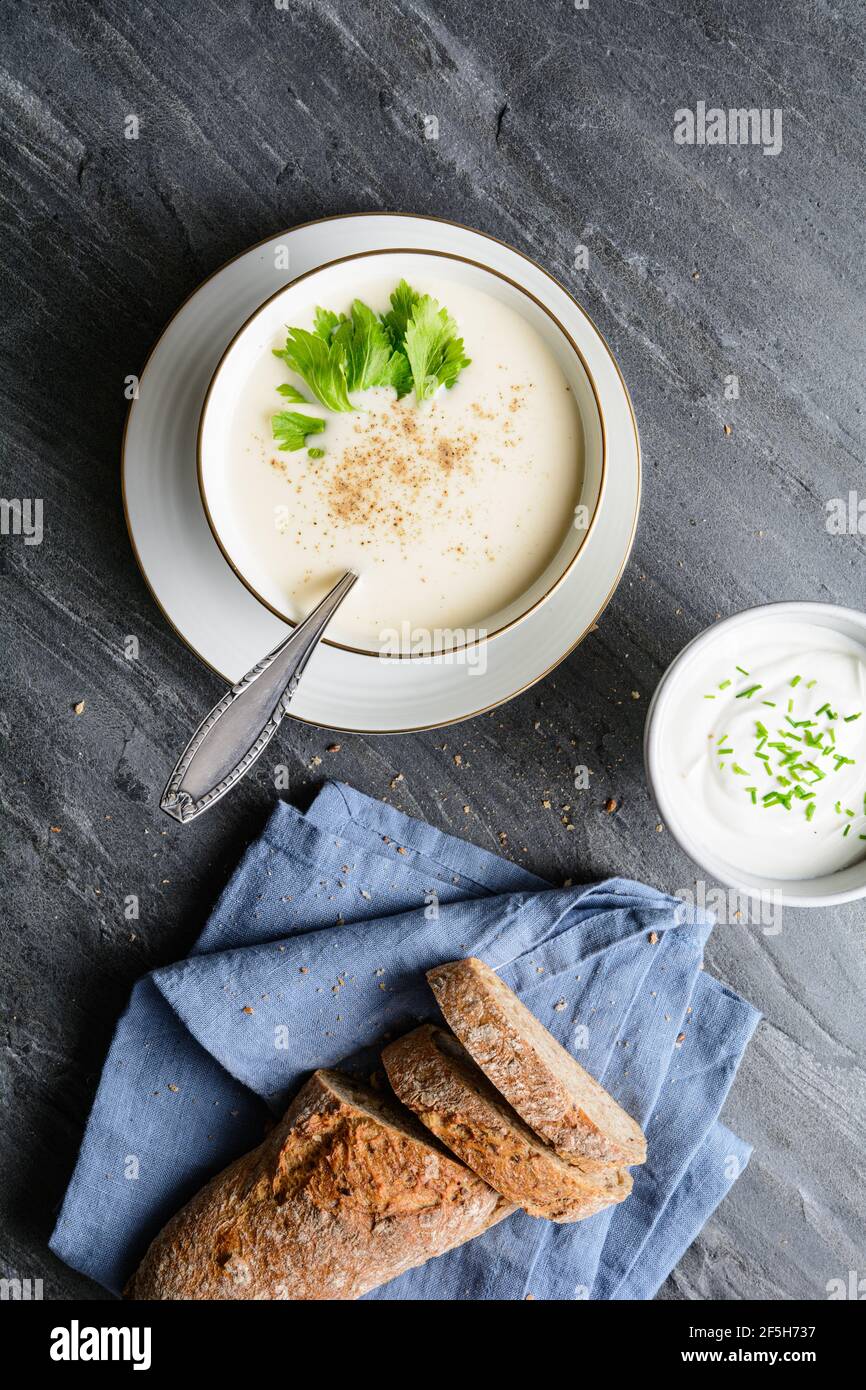 Köstliche cremige Sellerie-Suppe mit schwarzem Pfeffer und frischen Blättern, serviert mit knusprigem Brot, auf rustikalem Stein Hintergrund Stockfoto