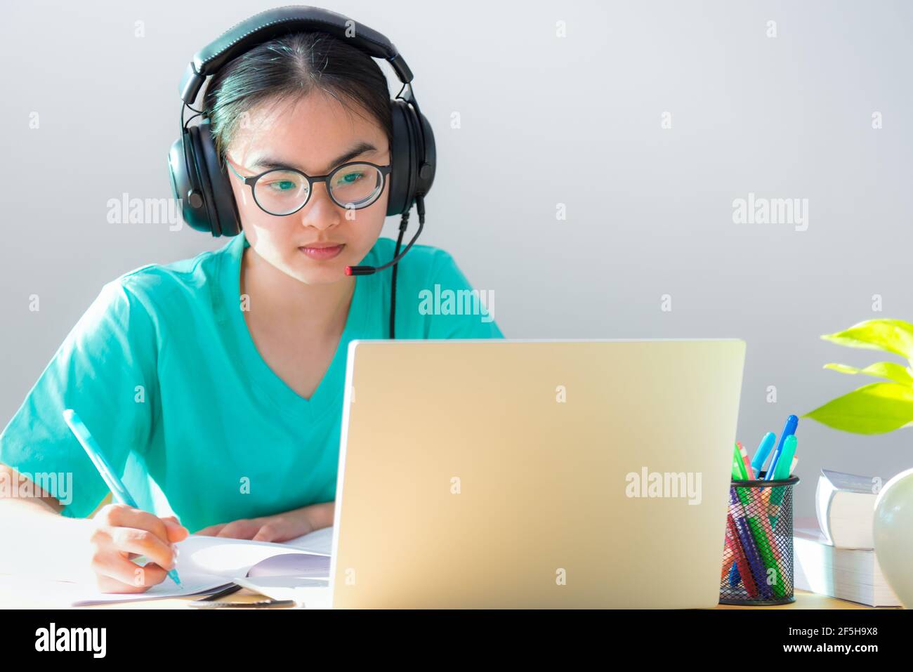 Asiatische junge Frau Student mit Brille Kopfhörer Studie ernst schreiben Anmerkung zu einer buchaussehenden Videokonferenz auf einem Laptop-Computer universitätsklasse ein Stockfoto