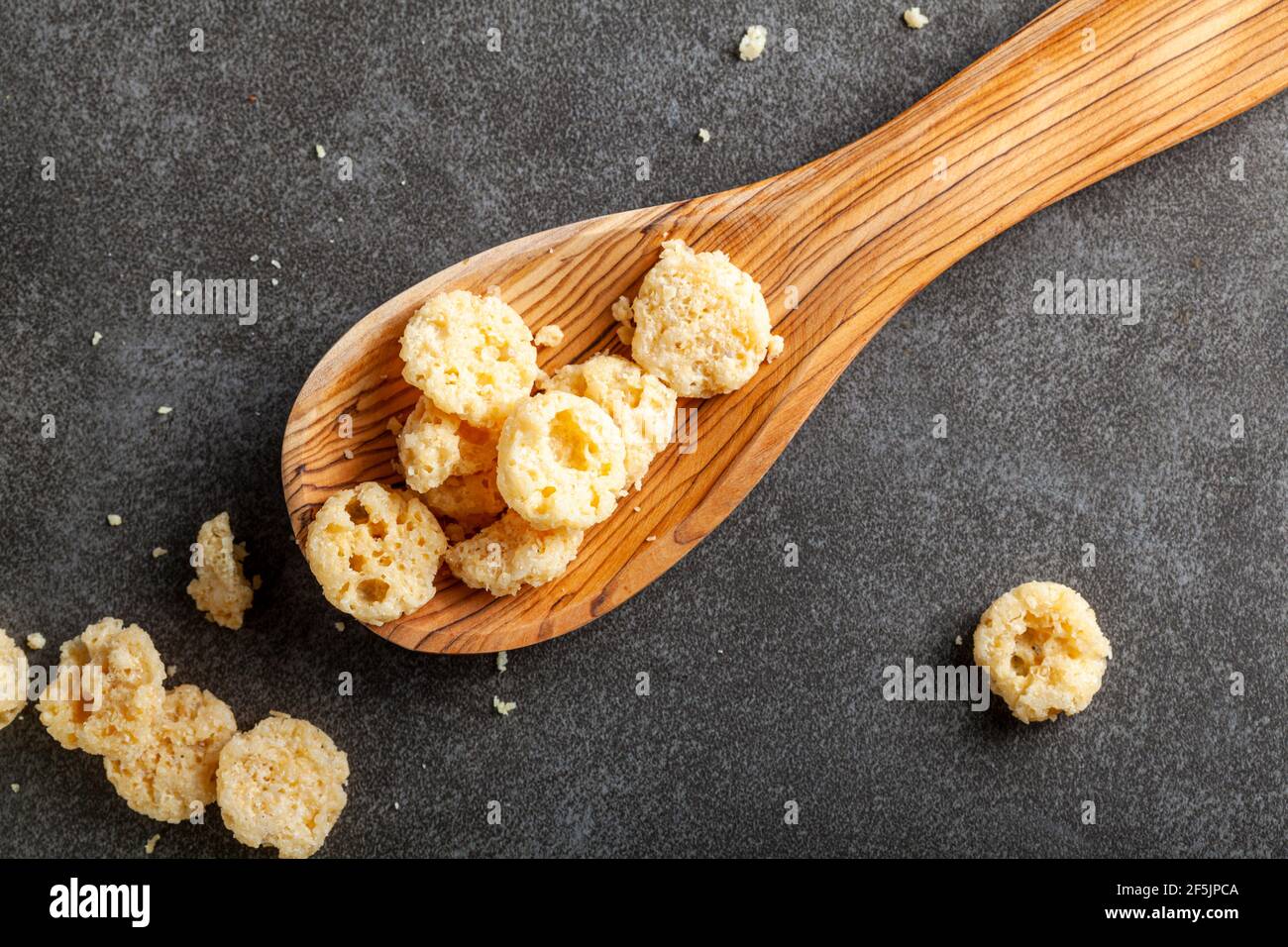 Im Ofen gebackener Käse beißt in einem Holzlöffel vor dunklem Hintergrund. Diese knusprigen leckeren Snacks eignen sich gut zum Naschen, auch für zusätzlichen Geschmack in Suppen Stockfoto