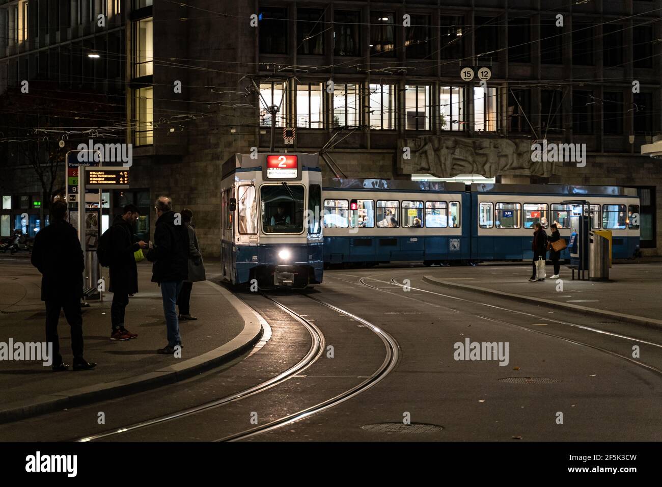 Zürich, Schweiz - Oktober 27 2020: An der Haltestelle Parade Platz im Herzen des Zürcher Geschäftsviertels warten die Menschen nachts auf eine Straßenbahn. Stockfoto