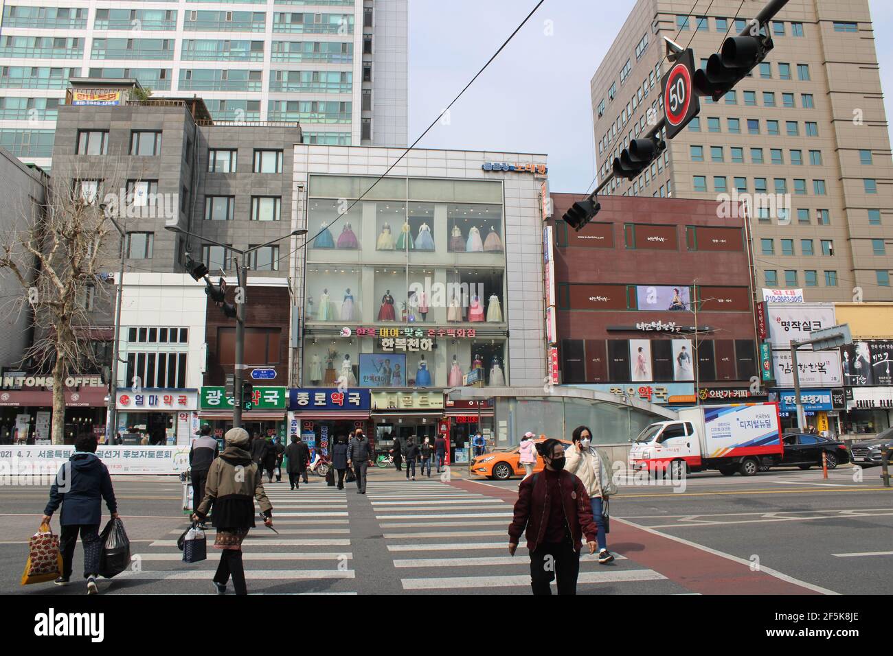Menschen in Masken überqueren Kreuzung in der Nähe der traditionellen koreanischen Bekleidungsgeschäft Stockfoto
