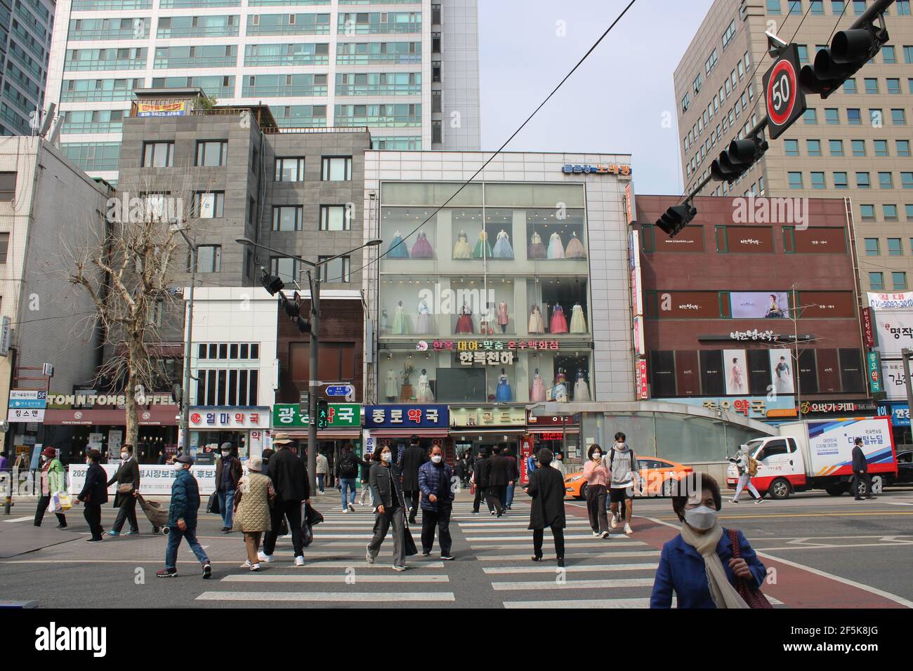 Menschen in Masken überqueren Kreuzung in der Nähe der traditionellen koreanischen Bekleidungsgeschäft Stockfoto