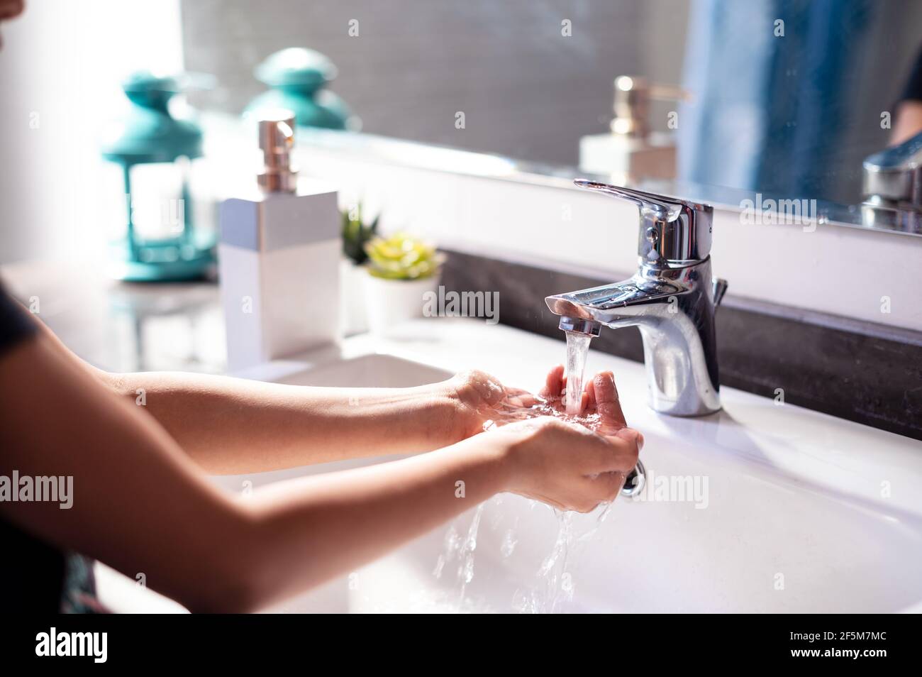 Ein junges Mädchen, das während der Covid-19-Pandemie die Hände über einem Waschbecken mit fließendem Wasser wascht, um sich vor dem gefährlichen Corona-Virus zu schützen. Stockfoto