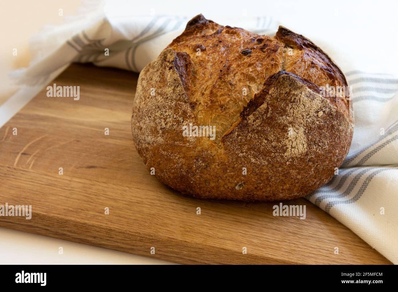 Frisch gebackenes selbstgebackenes Brot eingewickelt in weißes Leinentuch liegend Auf einem Holztisch Stockfoto