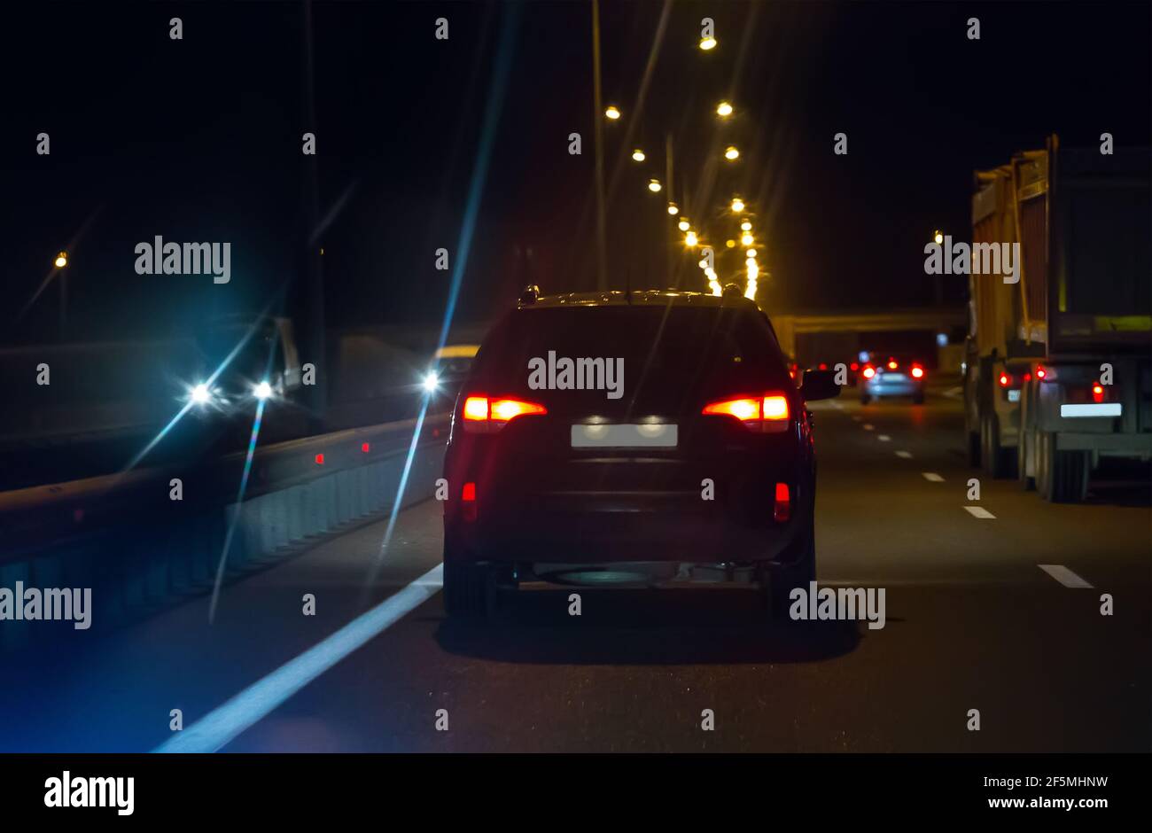 Autos mit Licht bewegen sich auf breiter mehrspuriger Straße bei Nacht. Rückansicht. Stockfoto
