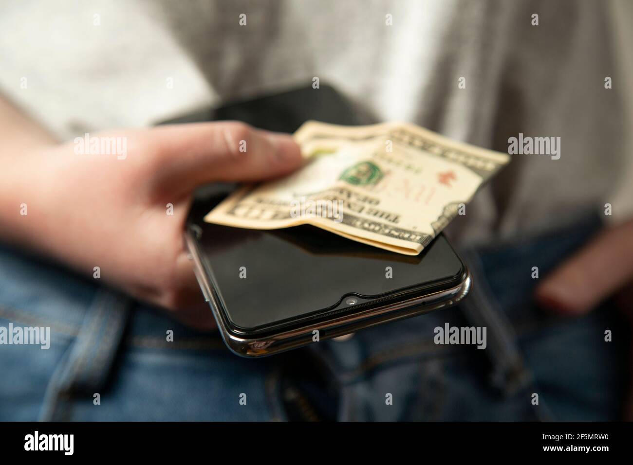 Das Mädchen hält Geld und ein Telefon in der Hand. Die Frau hat Bargeld und ein Handy in der Hand. Im Nahbereich. Moderne Technologien. Stockfoto