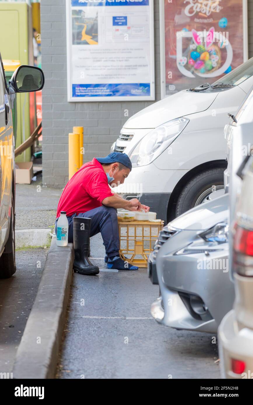 Ein junger vietnamesischer Australier sitzt auf einem städtischen Parkplatz und ruht sein Mittagessen auf einer umgedrehten Milchkiste in Cabramatta, Sydney, Australien Stockfoto