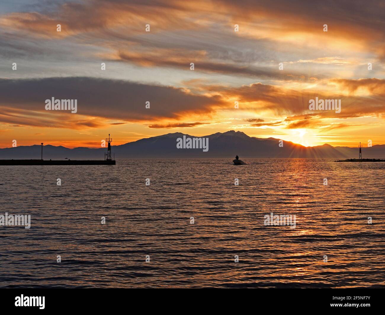 Epanomi, Thessaloniki, Griechenland. Ormos Epanomis, der Eingang des Docks bei Sonnenuntergang und ein Fischerboot, das einfährt Stockfoto