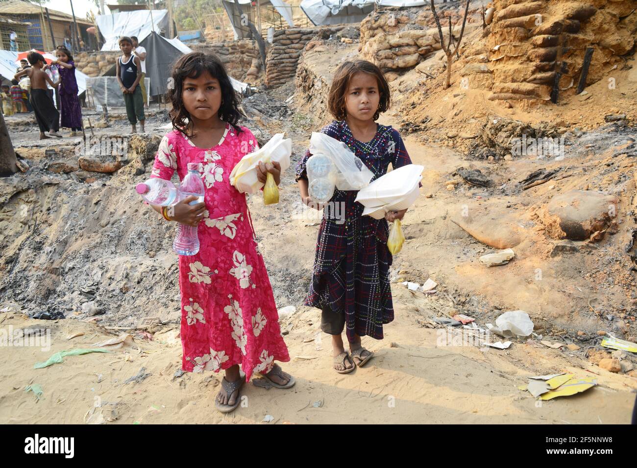 Kinder werden beobachtet, wie sie Lebensmittel nehmen, die von NGOs und sozialen Organisationen bereitgestellt wurden, Tage nach einem Brand in einem Flüchtlingslager in Ukhia, im südöstlichen Cox's B Stockfoto