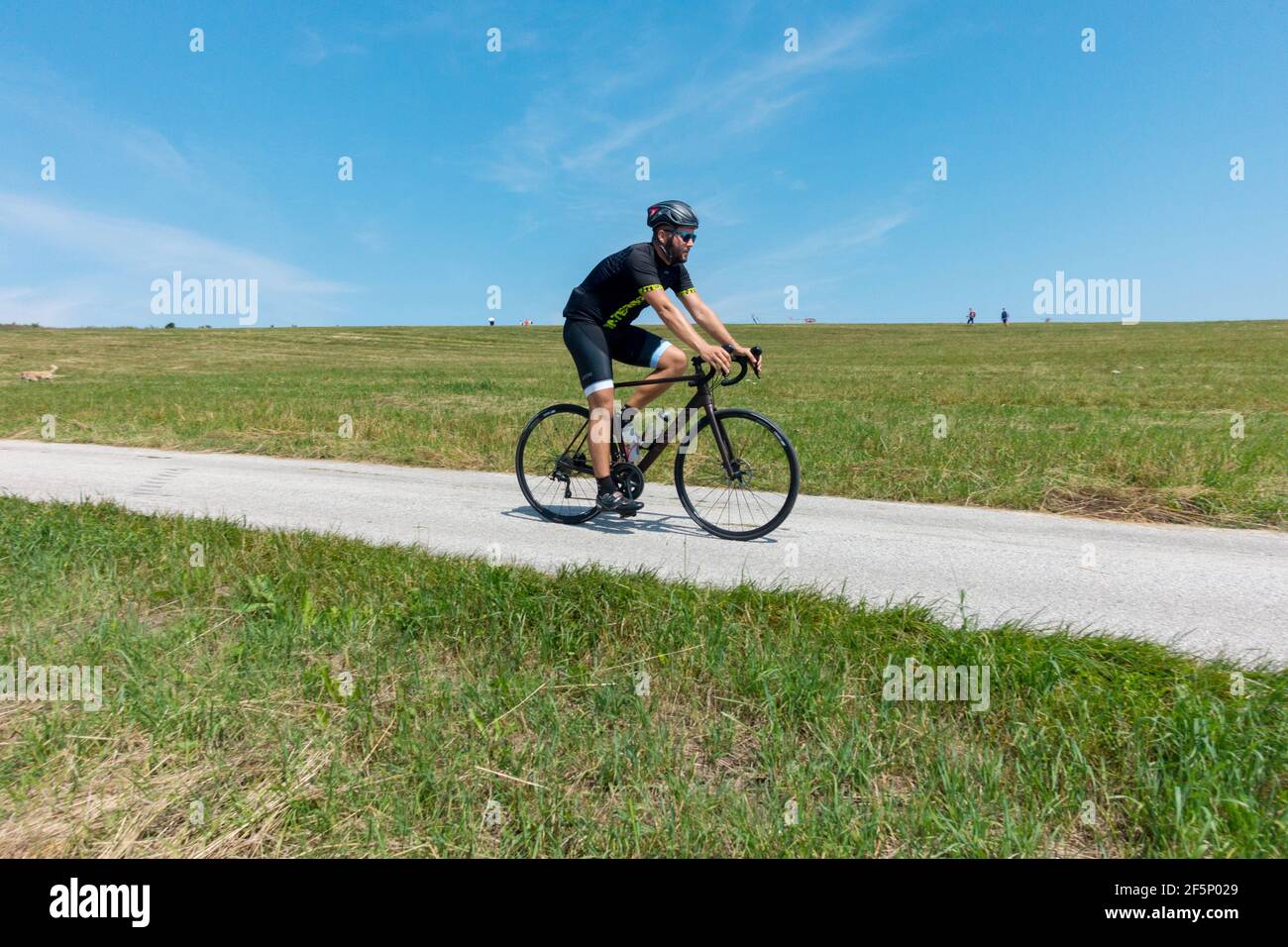 Einzelradfahrer auf Landstraße, aktiver Lebensstil, Mann, der alleine Fahrrad fährt, Radszene Stockfoto