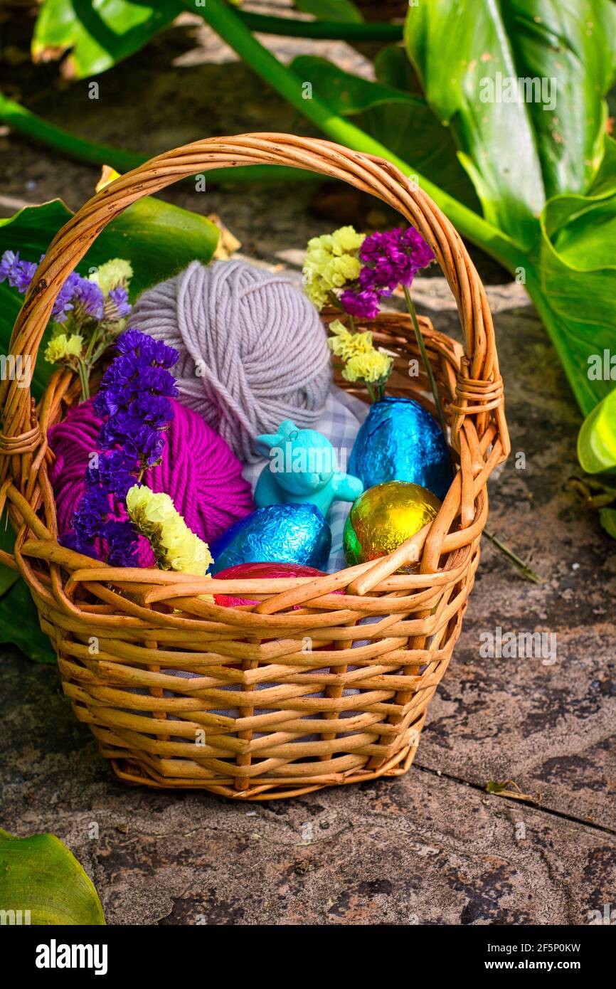 Ein Korb für eine Eiersuche dekoriert. Es hat Eier in Farbe Zinnfolie eingewickelt, ein Spielzeug von einem Kaninchen und einige Kugeln aus Garn. Es ist von Vegetation umgeben, cl Stockfoto