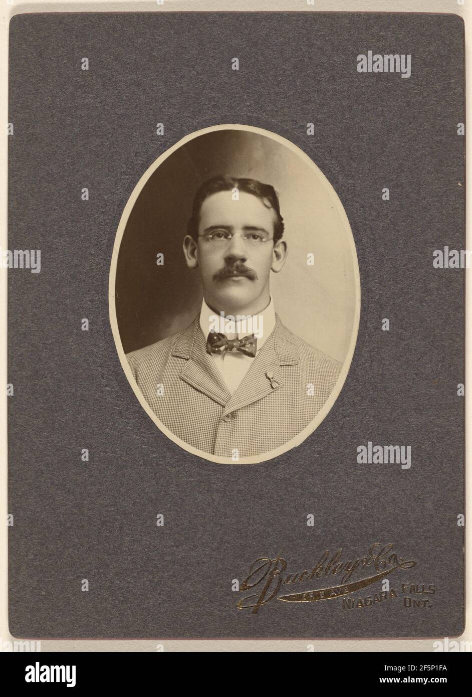 Nicht identifizierter Mann mit Schnurrbart, der eine Brille mit Drahtumrandung trägt. Buckley & Company Stockfoto