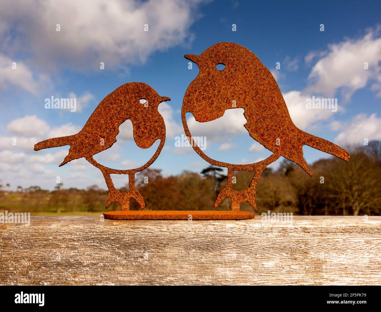 Ein dekoratives Paar Rotkehlchen lasergeschnitten aus rostfreiem Stahl Montiert auf einem Holzsockel mit heller Wolke und blau Himmel dahinter Stockfoto