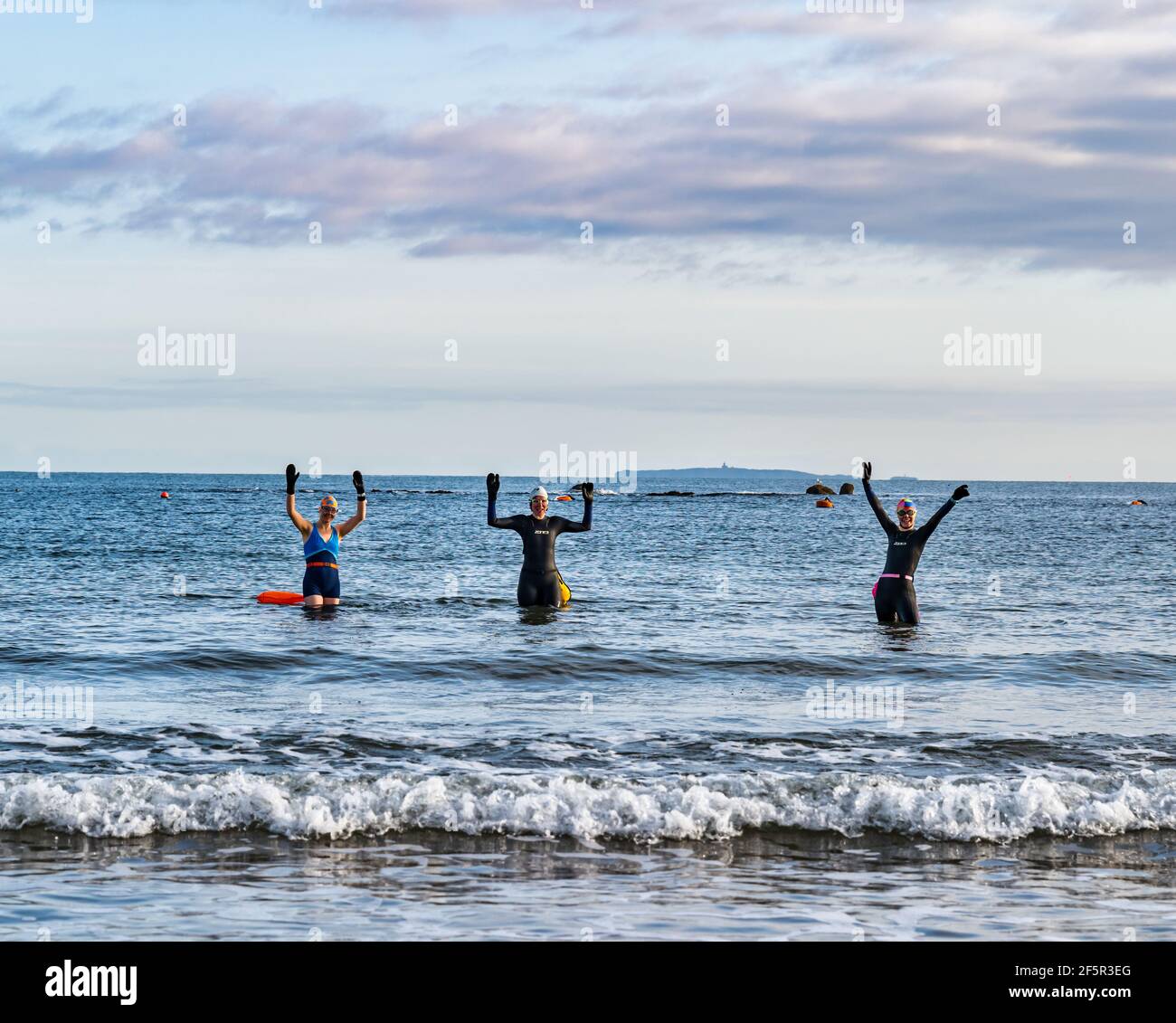 Wildwasser- oder Freiwasser-Schwimmerinnen in Neoprenanzügen betreten Firth of Forth Sea mit ausgestreckten Armen, North Berwick, East Lothian, Schottland, Großbritannien Stockfoto