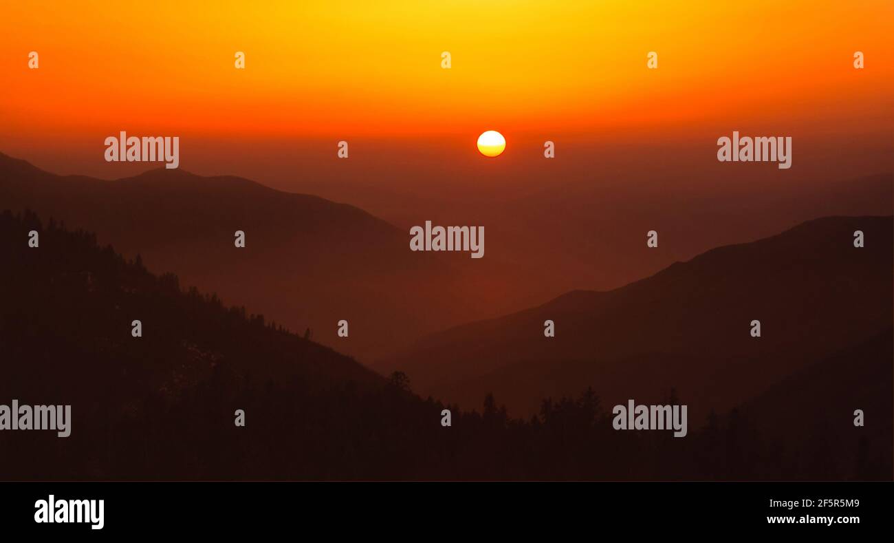 Heller Sonnenuntergang mit einer großen gelben Sonne über den Hügeln. Stockfoto