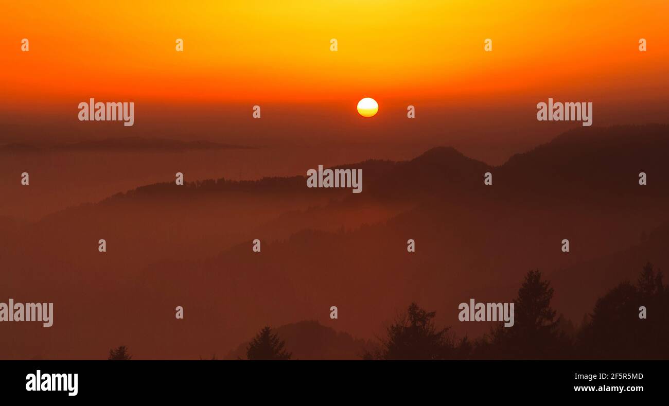Heller Sonnenuntergang mit einer großen gelben Sonne über den Hügeln. Stockfoto