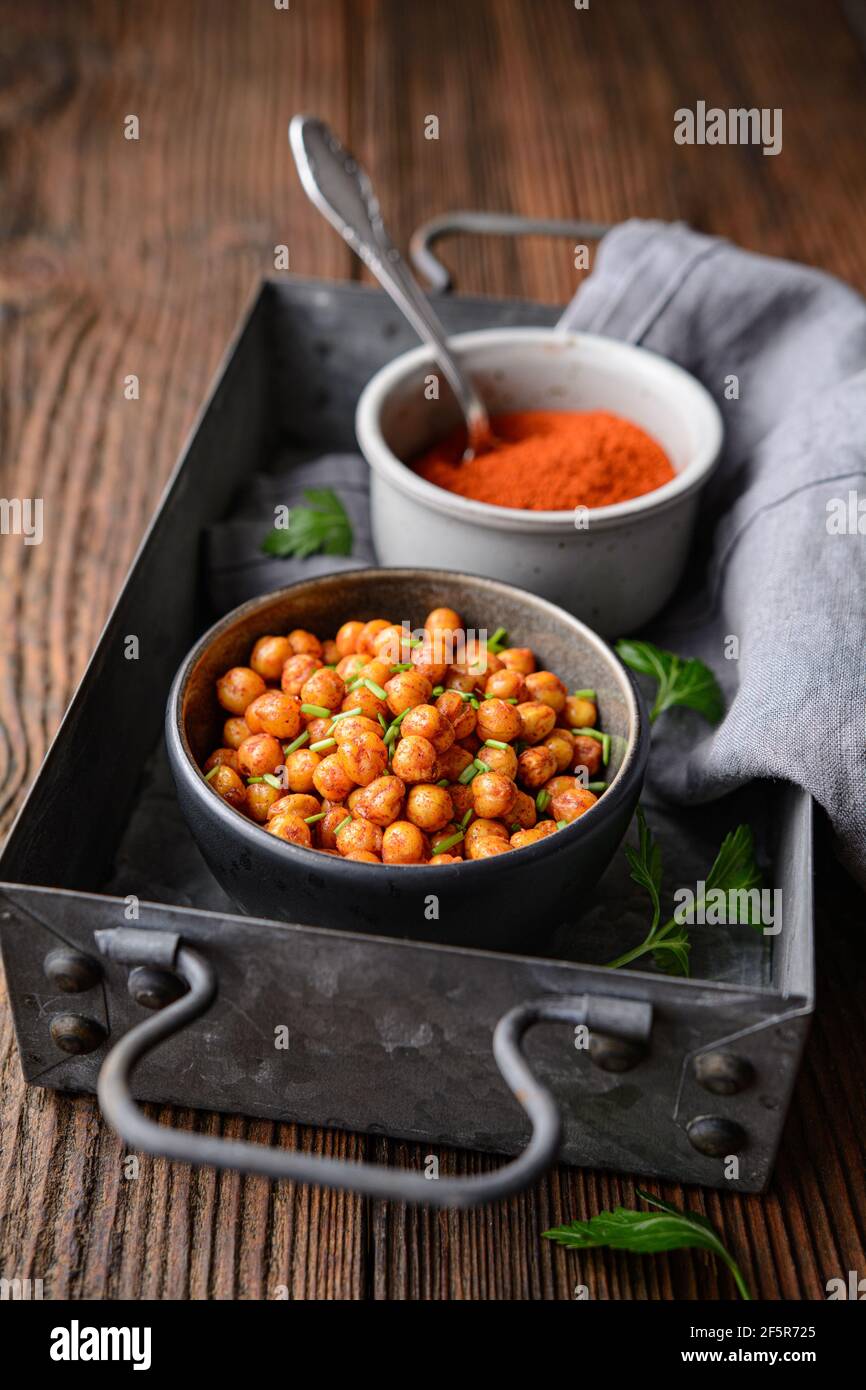 Knackiger Snack, knusprig und würzig im Ofen geröstete Kichererbsen mit Paprika und rotem Chilipulver auf rustikalem Holzhintergrund Stockfoto