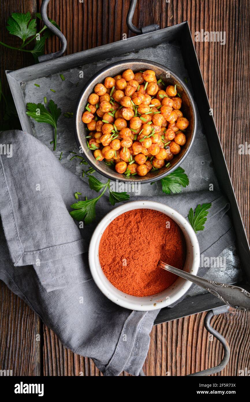 Knackiger Snack, knusprig und würzig im Ofen geröstete Kichererbsen mit Paprika und rotem Chilipulver auf rustikalem Holzhintergrund Stockfoto