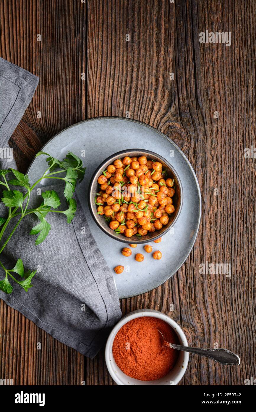 Knackiger Snack, knusprig und würzig im Ofen geröstete Kichererbsen mit Paprika und rotem Chilipulver auf rustikalem Holzhintergrund Stockfoto