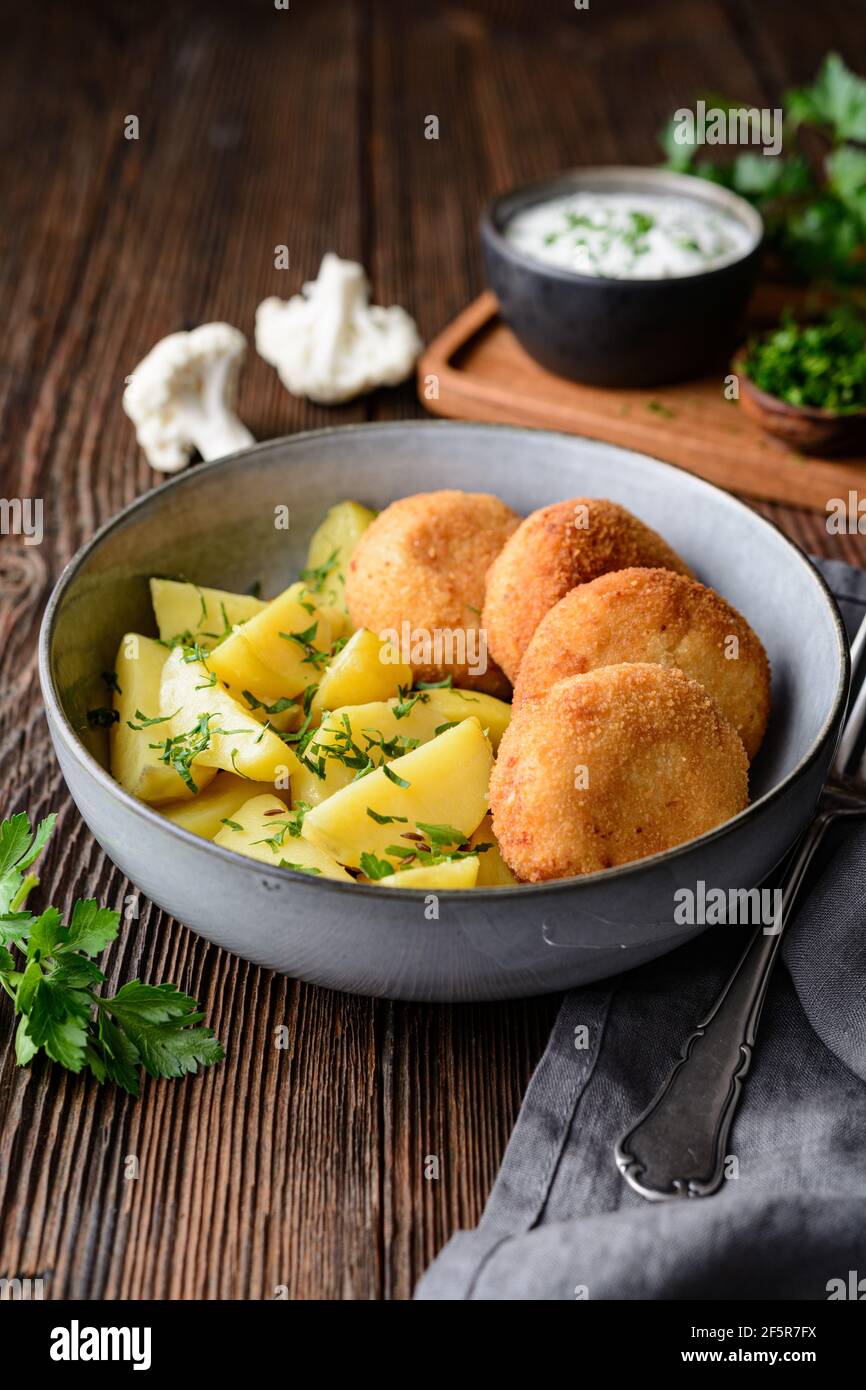 Gebratener Blumenkohl- und Käsebroketten mit gekochten Kartoffeln und sauer Creme Dip auf rustikalem Holzhintergrund Stockfoto