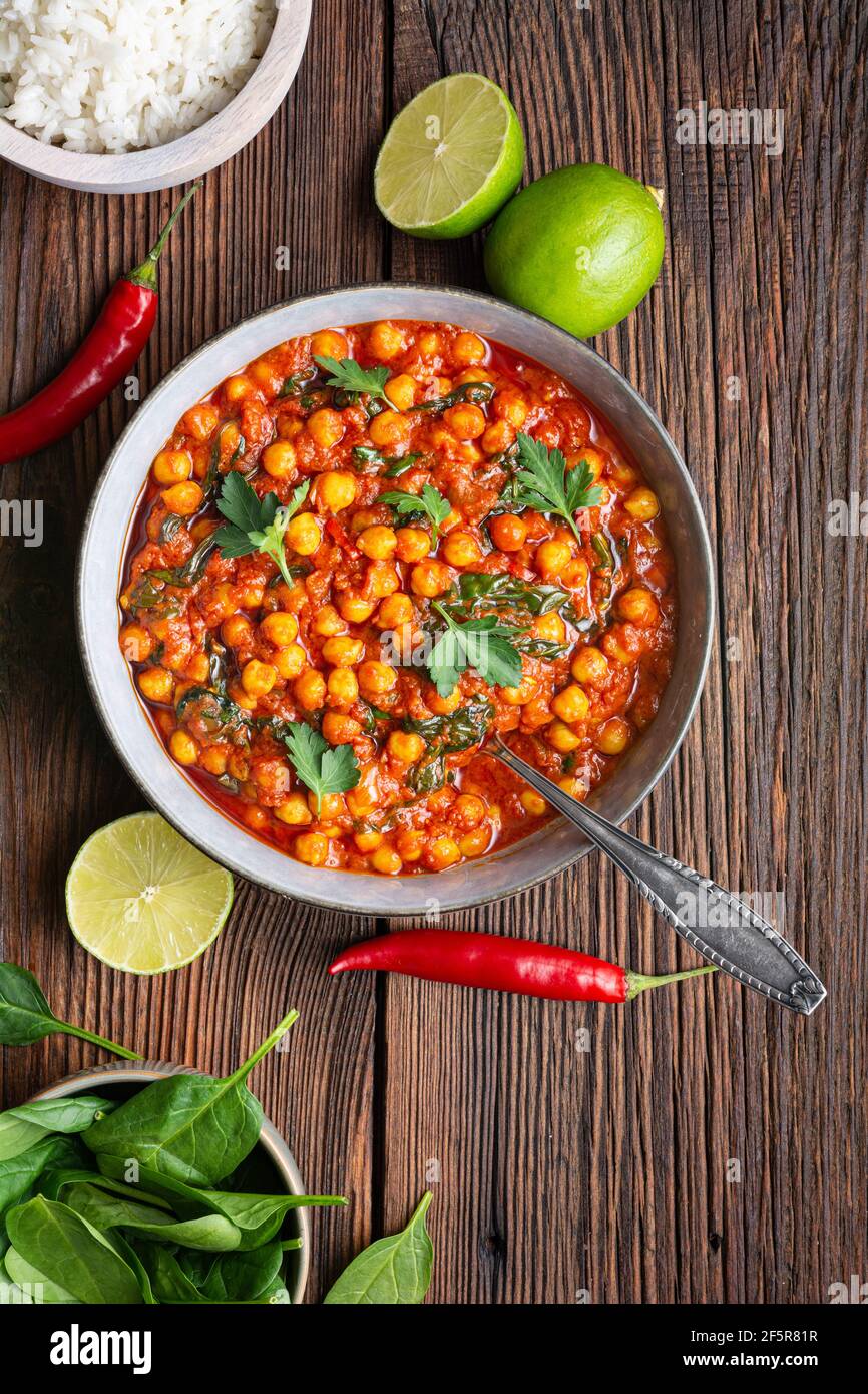 Indische Mahlzeit, würziges Kichererbsencurry mit Spinat in einer Schüssel serviert mit Reis auf rustikalem Holzhintergrund Stockfoto