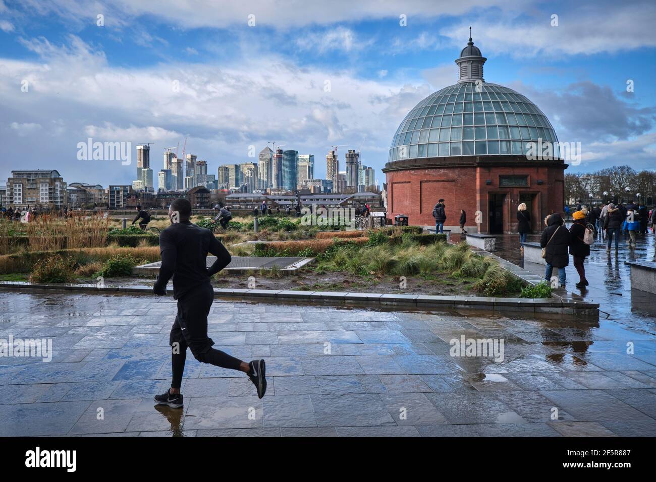 Mann, der auf einem nassen Pfad in Greenwich läuft. London. Finanzviertel Canary Wharf im Hintergrund. Stockfoto