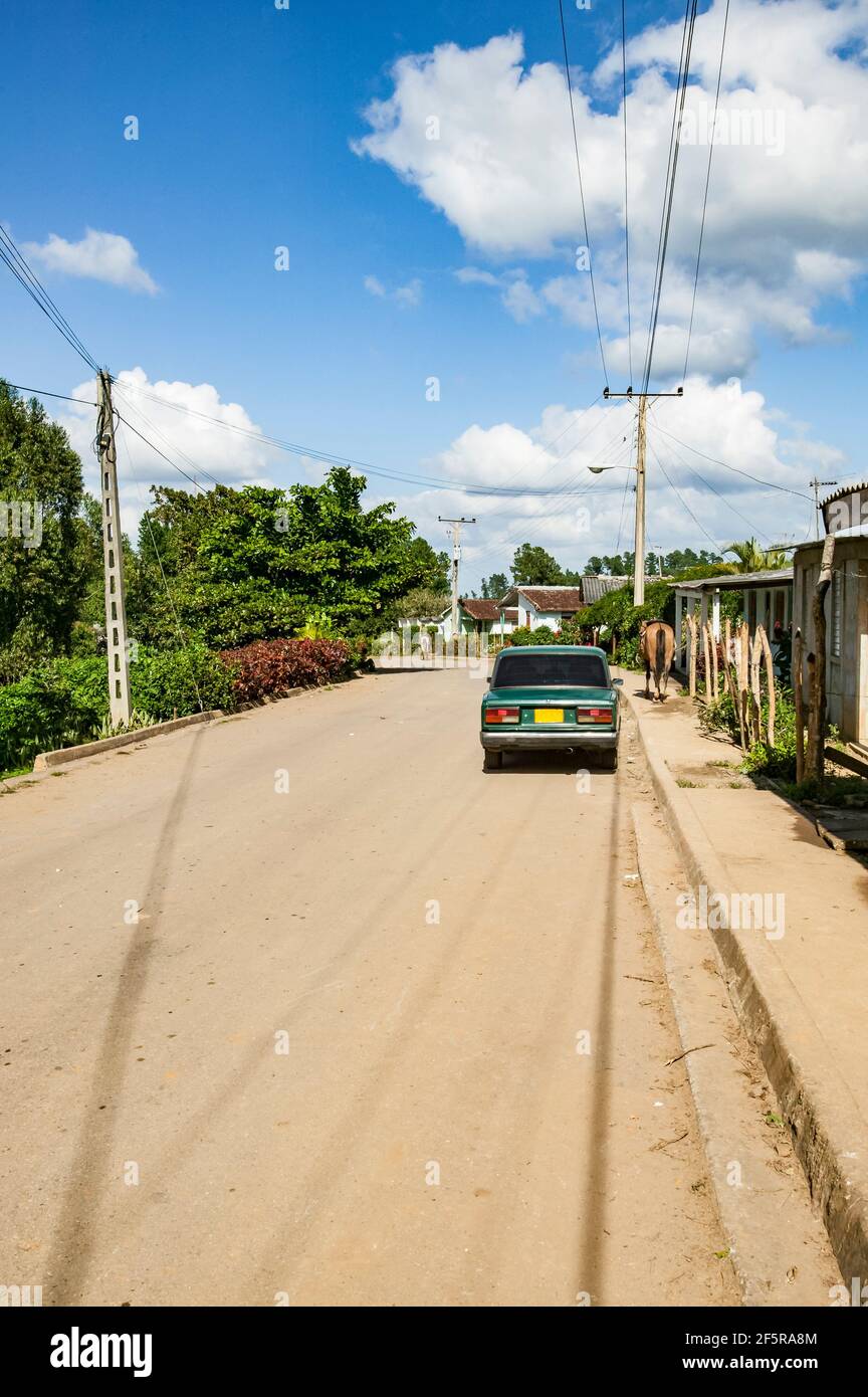 Ein grünes Auto parkte neben einem braunen Pferd, das auf dem Seitenweg an einem Holzpfosten in einem ländlichen kubanischen Dorf in der Provinz Cienfuegos, Kuba, stand Stockfoto