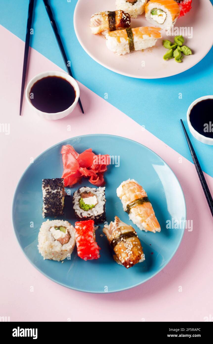 Leckere Sushi-Brötchen auf blauem Teller mit Saucen, Essstäbchen, Ingwer und Wasabi auf farbigem Hintergrund. Sushi-Menü. Lieferservice Japanisches Essen . Wie Stockfoto