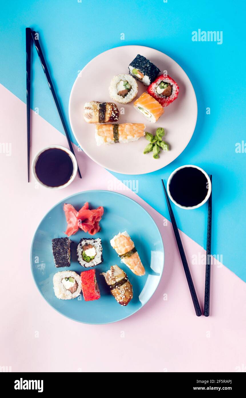 Leckere Sushi-Brötchen auf blauem Teller mit Saucen, Essstäbchen, Ingwer und Wasabi auf farbigem Hintergrund. Sushi-Menü. Lieferservice Japanisches Essen . Wie Stockfoto