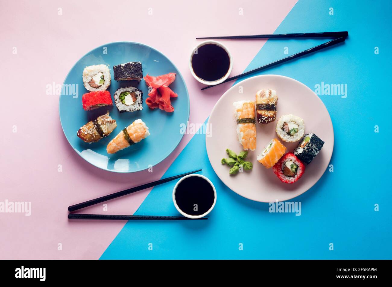 Leckere Sushi-Brötchen auf blauem Teller mit Saucen, Essstäbchen, Ingwer und Wasabi auf farbigem Hintergrund. Sushi-Menü. Lieferservice Japanisches Essen . Wie Stockfoto