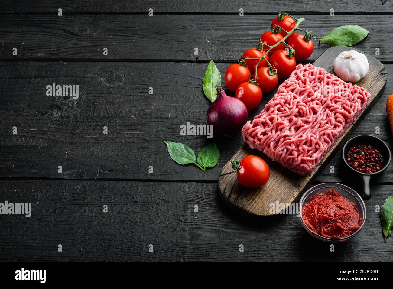 Zutaten für Bolognese-Sauce, Hackfleisch, Tomaten, Kräuter-Set, auf Holzschneidebrett, auf schwarzem Holztisch-Hintergrund, mit Platz für Kopien Stockfoto