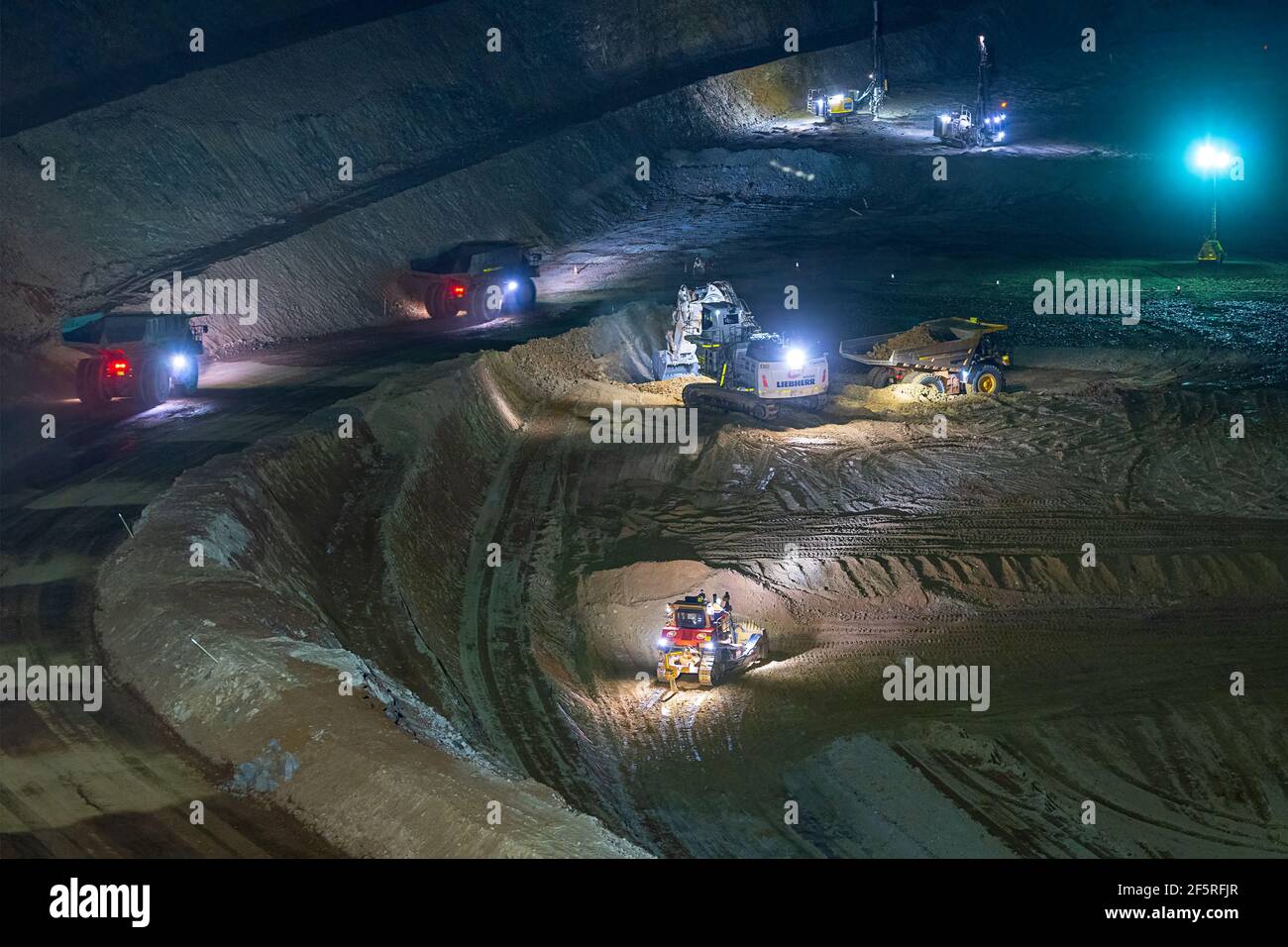 Tagebaubetrieb in der Nacht mit Bohrgeräten, Muldenkipper und Ladern, die unter Flutlicht betrieben werden. Stockfoto