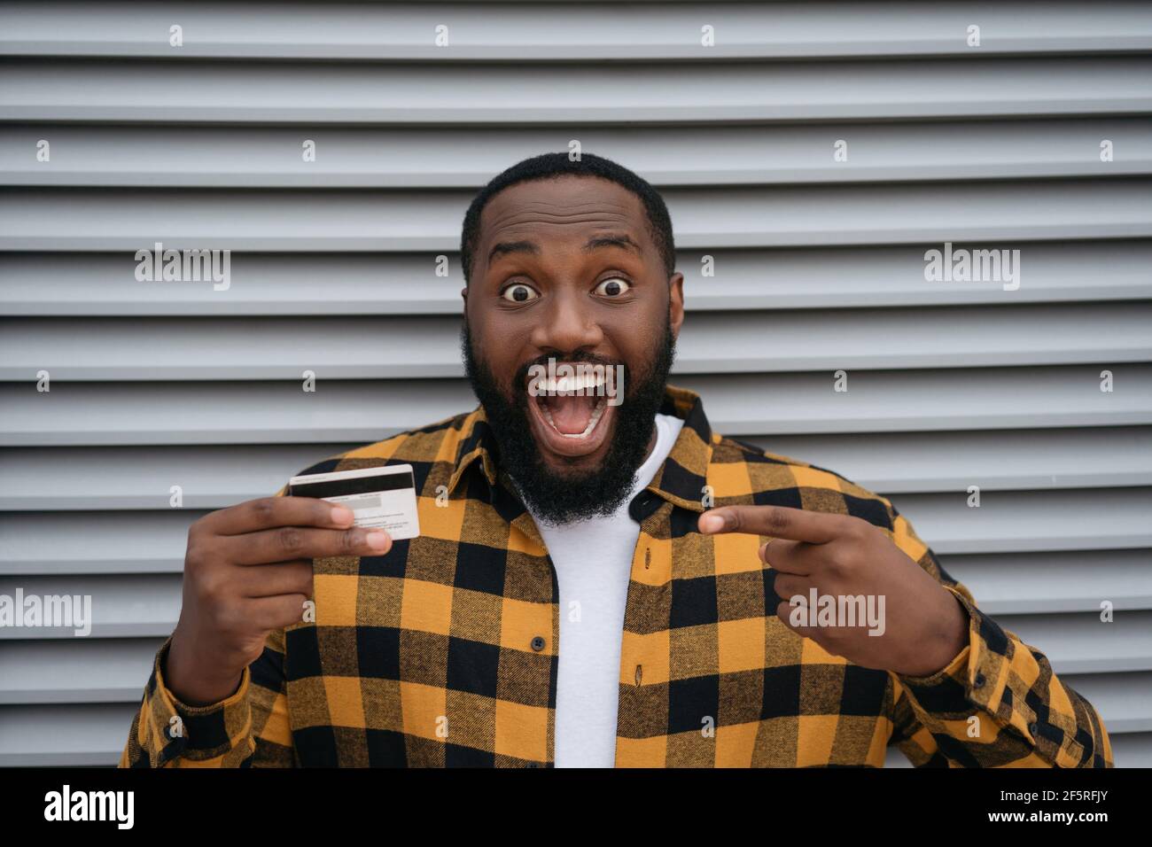 Emotionaler afroamerikanischer Mann mit Kreditkarte, isoliert auf grauem Hintergrund Stockfoto