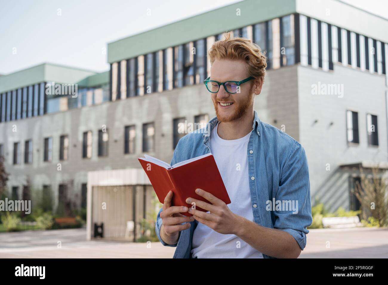 Schöner lächelnder Mann, der im Freien Buch liest. Erfolgreiche Studenten tragen stilvolle Brillen studieren, Prüfungsvorbereitung, Bildungskonzept Stockfoto