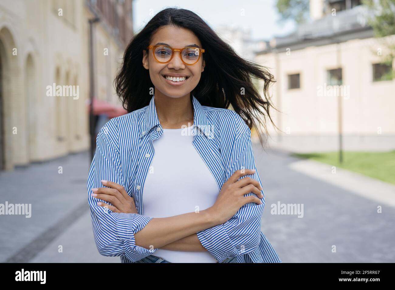 Porträt einer schönen lächelnden afroamerikanischen Frau, die auf die Kamera schaut und auf der Straße steht. Junge selbstbewusste Geschäftsfrau posiert für Bilder Stockfoto