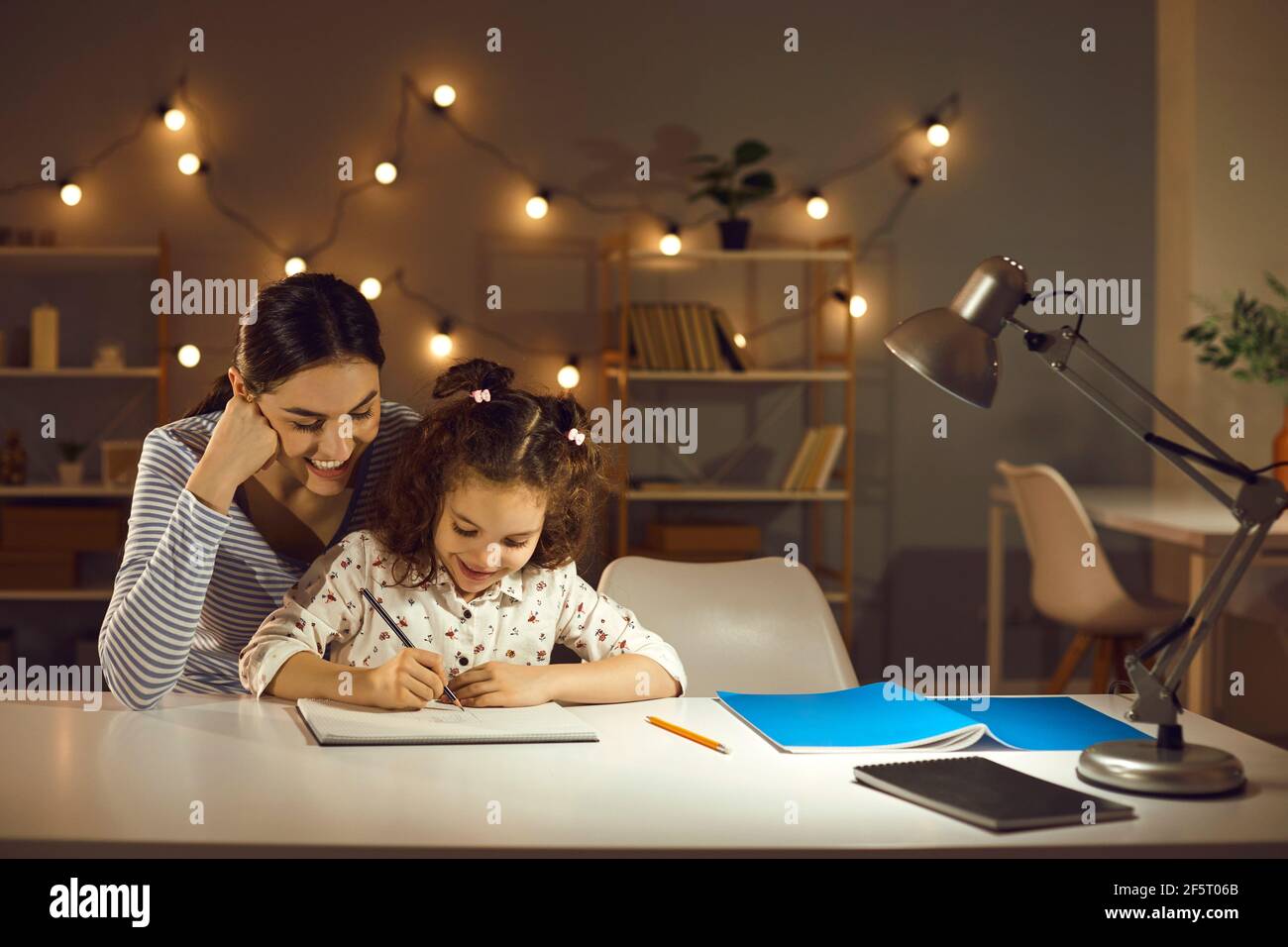 Glückliche Mutter und Tochter machen Hausaufgaben sitzen am Schreibtisch in Gemütliches Zimmer am Abend Stockfoto