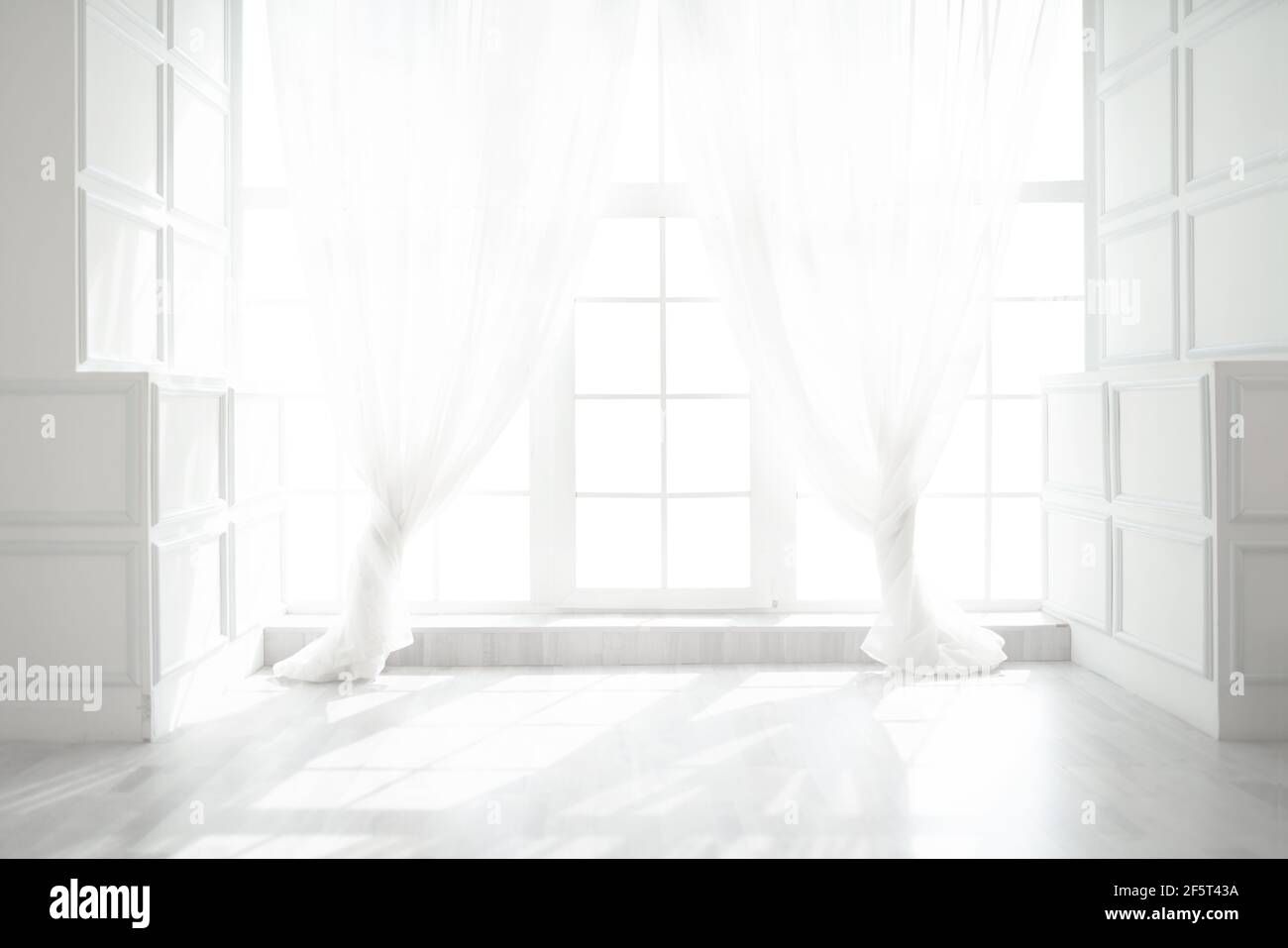 Hintergrundbeleuchtetes Fenster mit weißen Vorhängen im leeren Raum Stockfoto