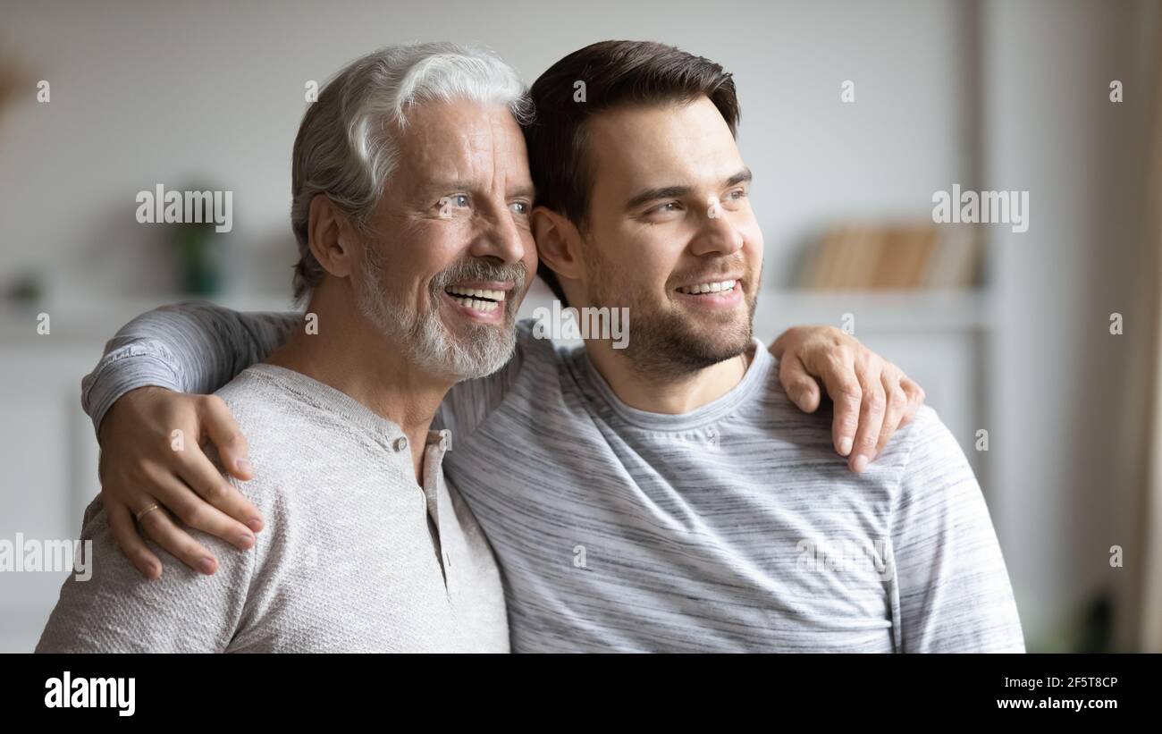 Lächelnder älterer Vater und erwachsener Sohn blicken in die Ferne Stockfoto