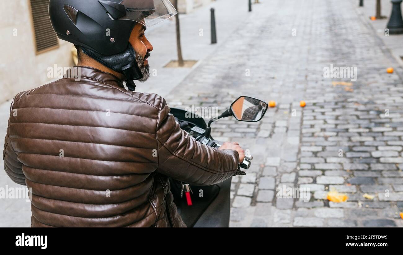 Rückansicht von brutalen ethnischen männlichen Biker in Helm fahren Modernes Motorrad, während Sie weit in die Stadt schauen Stockfoto