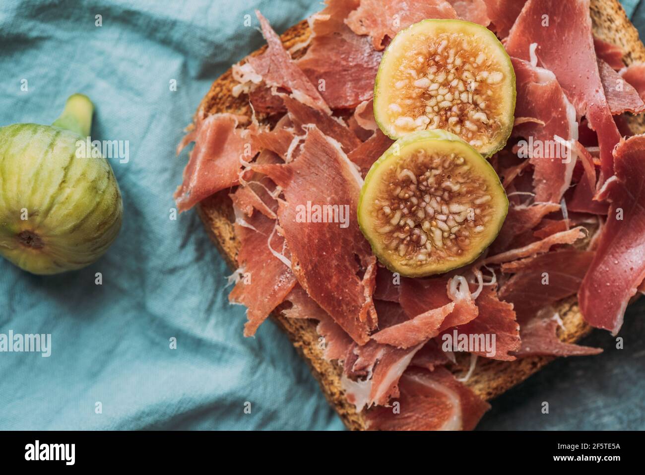 Köstlicher Toast mit Iberico Schinken, Käse und frischen Feigen auf der blauen Tischdecke, köstliche Vorspeise, ideal als Aperitif. Gesunde Ernährung Stockfoto