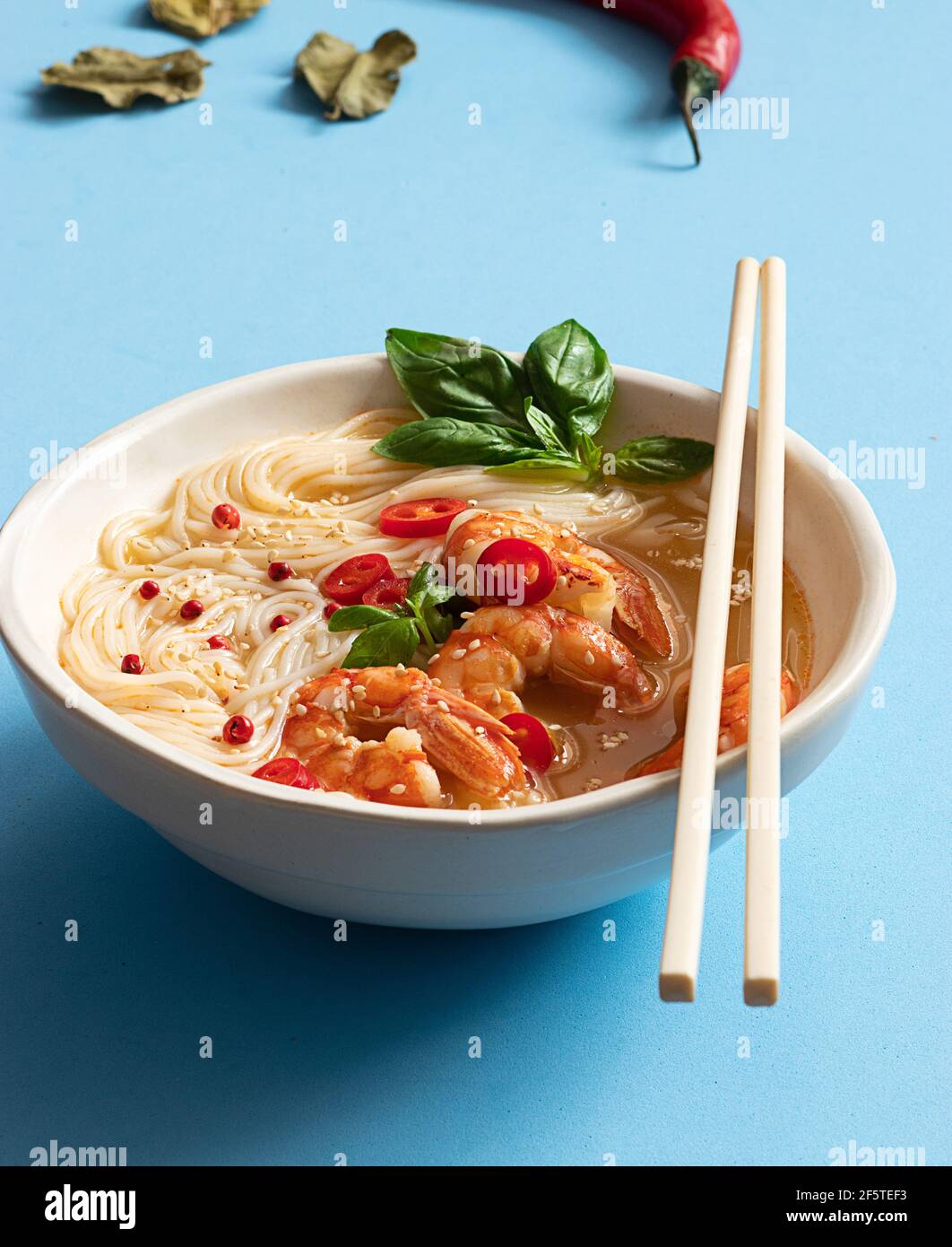 Tom Yum Suppe in Schüssel mit Essstäbchen auf blauem Hintergrund Stockfoto