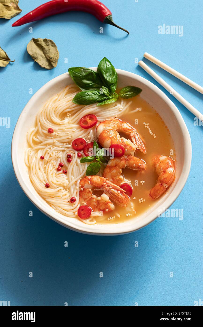 Tom Yum Suppe in Schüssel mit Essstäbchen auf blauem Hintergrund Stockfoto